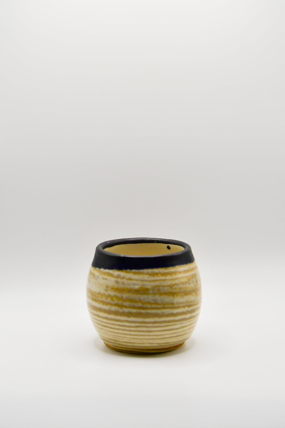 Small ceramic cup with ribbed texture and black rim on a white background
