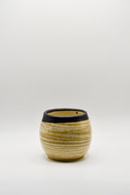 Small ceramic cup with ribbed texture and black rim on a white background