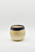 Small ceramic cup with ribbed texture and black rim on a white background