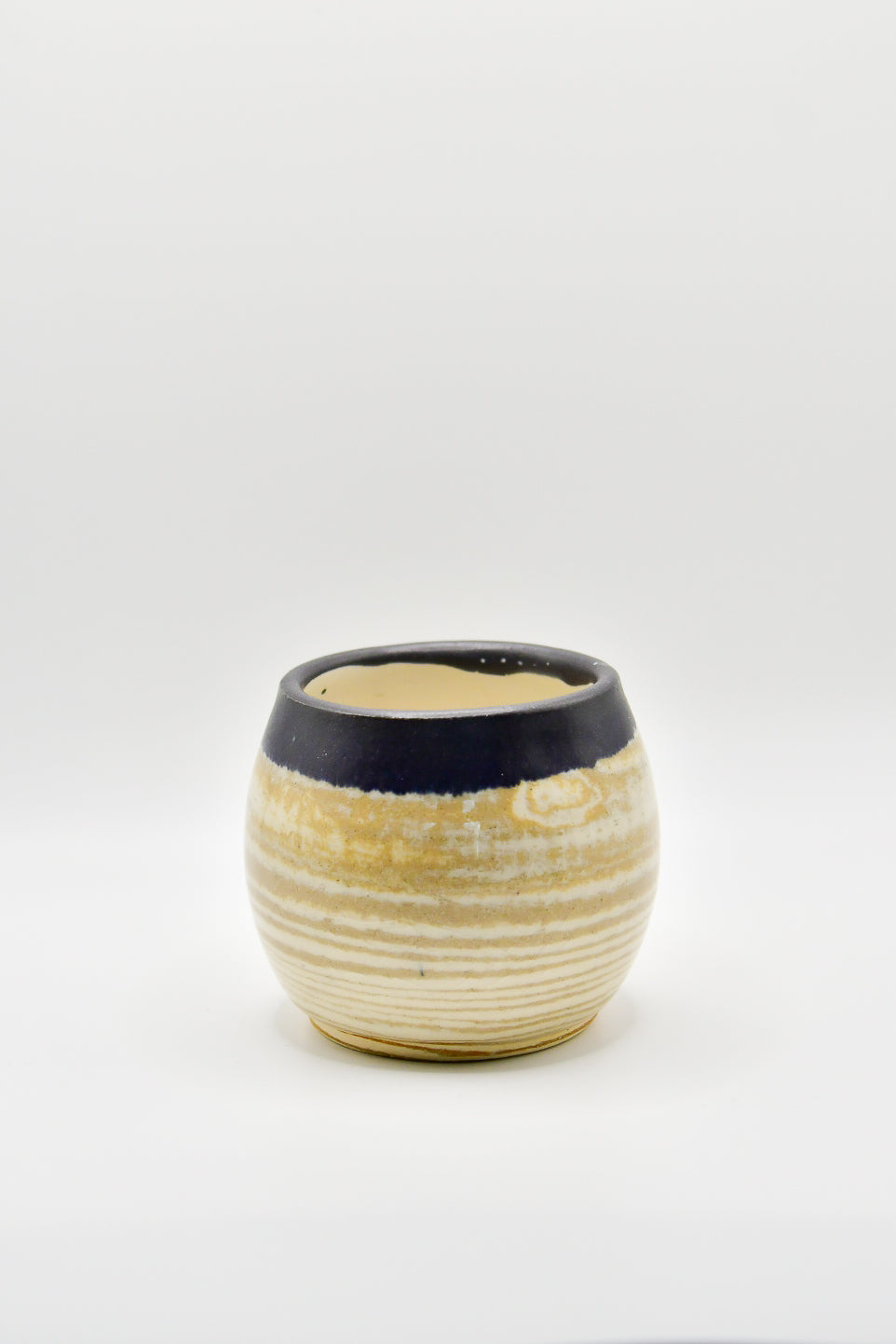 Small ceramic cup with ribbed texture and black rim on a white background